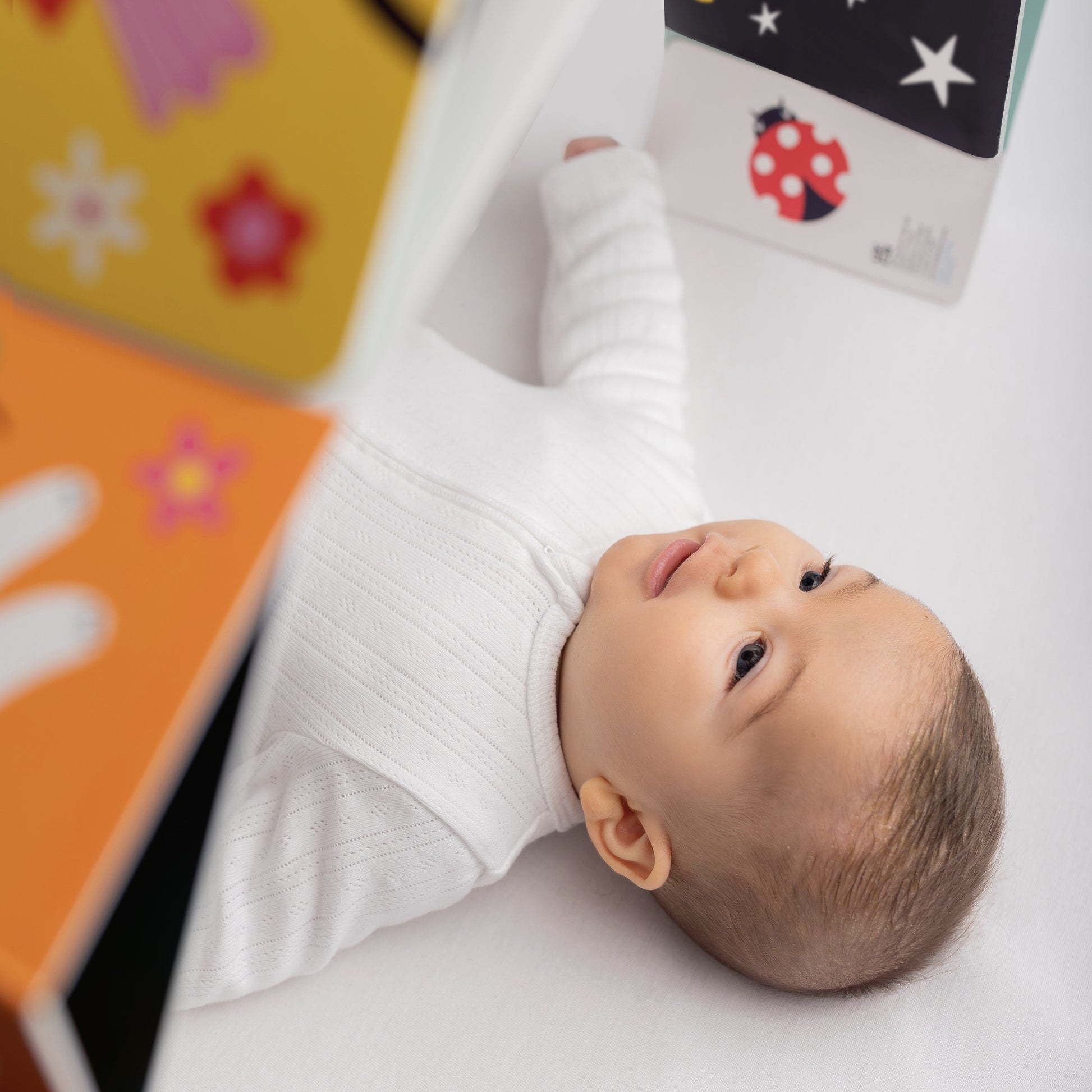 Baby lying on a white surface with colorful baby sensory arch around